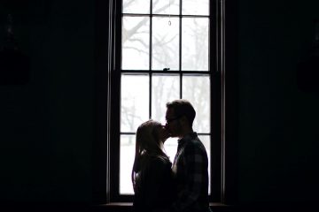 Two people kissing in front of a window.